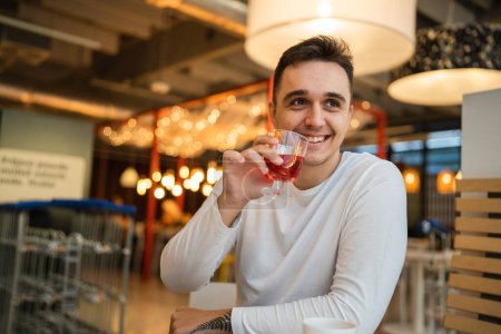 Foto de Un hombre joven adulto caucásico macho sentarse solo en la mesa en la cafetería o restaurante beber fruta espumoso agua copia espacio real gente feliz sonrisa - Imagen libre de derechos