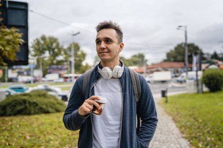 Photo for One young adult caucasian man walking in the city or town near park with cup of coffee in autumn or spring day happy male tourist standing alone real people copy space - Royalty Free Image