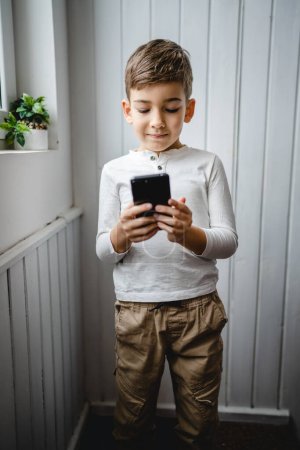 one boy caucasian child preschooler hold smartphone mobile phone at home play video games childhood and growing up technology addiction concept use smartphone app for online browsing or watch video