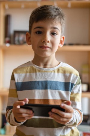 Téléchargez les photos : One boy caucasian child preschooler hold smartphone mobile phone at home play video games childhood and growing up technology addiction concept use smartphone app for online browsing or watch video - en image libre de droit