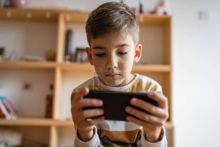 Photo for One boy caucasian child preschooler hold smartphone mobile phone at home play video games childhood and growing up technology addiction concept use smartphone app for online browsing or watch video - Royalty Free Image