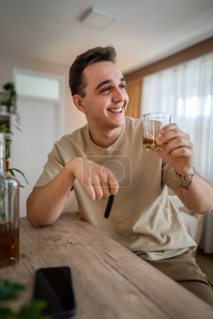 Téléchargez les photos : Un homme assis à la maison avec une bouteille d'alcool boire whisky alcoolique abus d'alcool, addiction et l'homme dépression concept boire et conduire copie espace tenir clés de voiture - en image libre de droit