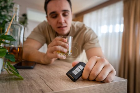 Téléchargez les photos : Un homme assis à la maison avec une bouteille d'alcool boire whisky alcoolique abus d'alcool, addiction et l'homme dépression concept boire et conduire copie espace tenir clés de voiture - en image libre de droit