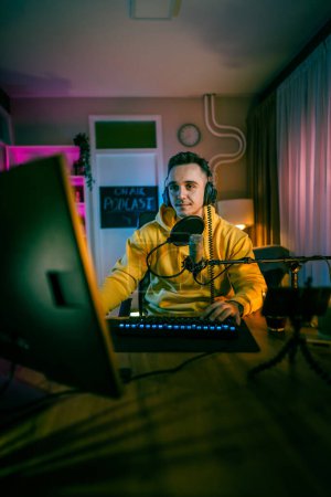 Photo for Young man play video games on pc computer while streaming to social media or internet online playtrough or walktrough video male gamer having fun at home wear headphone copy space - Royalty Free Image
