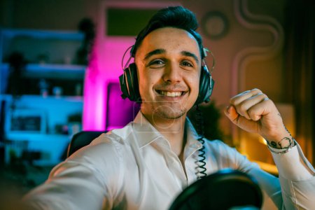 Téléchargez les photos : Autoportrait d'un homme caucasien mâle streamer blogueur ou créateur de contenu avec casque sur sa tête sourire heureux confiant dans son studio copie espace contenu généré par l'utilisateur UGC - en image libre de droit