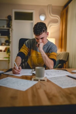 Photo for Young caucasian man teenager student study at home at the table at night or evening determinate learning prepare lesson or exam alone real people copy space - Royalty Free Image