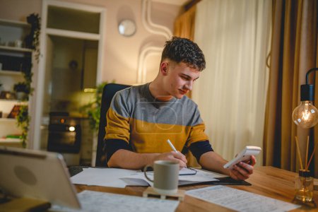 Photo for Young caucasian man teenager student study at home at the table at night or evening determinate learning prepare lesson or exam alone real people copy space - Royalty Free Image