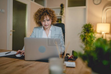 Photo for One woman caucasian female work while sit at the desk use laptop computer female entrepreneur or manager lawyer working at night confident prepare strategy and make plan real people copy space - Royalty Free Image