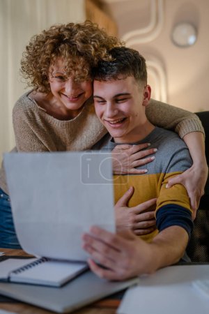 Photo for Young man and his mother woman hold paper read good news in letter sit at desk at home beautiful female received correspondence bank statement or notification invitation scholarship pleasant message - Royalty Free Image