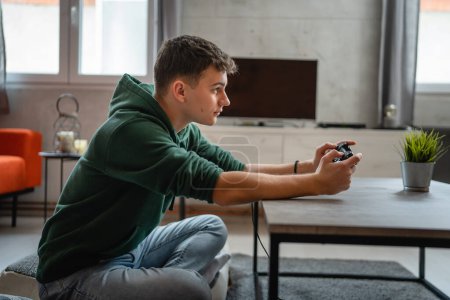 Téléchargez les photos : Un adolescent caucasien mâle jeune homme jouer console jeu vidéo à la maison - en image libre de droit