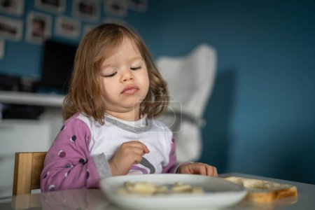 Photo for One girl small caucasian toddler female child eat at the table at home - Royalty Free Image