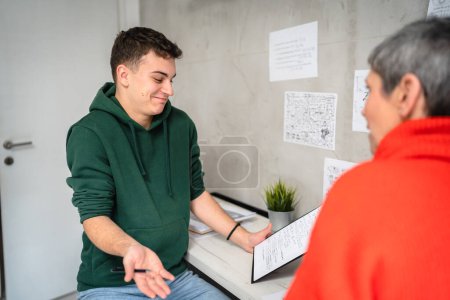 Foto de One student teenage caucasian man study learn with help of his tutor professor or mother senior woman at home having private lesson to prepare for exam education concept real people copy space - Imagen libre de derechos