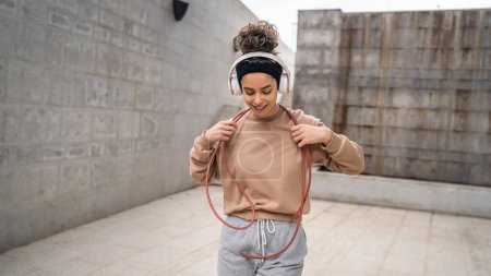 Photo for One woman young adult caucasian female jumping rope training concept beautiful sporty generation Z in day outdoor with headphones on her head copy space real person - Royalty Free Image