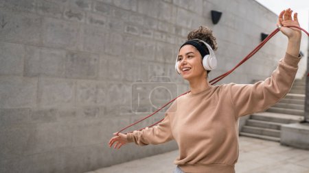 Foto de Una mujer joven adulto caucásico femenino saltar cuerda entrenamiento concepto hermosa generación deportiva Z en día al aire libre con auriculares en su cabeza copia espacio persona real - Imagen libre de derechos