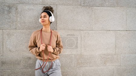 Téléchargez les photos : Une femme jeune adulte caucasien femme saut à la corde concept de formation belle génération sportive Z dans la journée en plein air avec écouteurs sur sa tête copie espace personne réelle - en image libre de droit