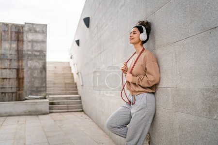 Photo for One woman young adult caucasian female jumping rope training concept beautiful sporty generation Z in day outdoor with headphones on her head copy space real person side view - Royalty Free Image