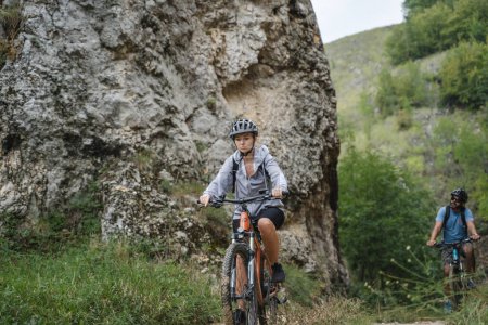 Téléchargez les photos : Femme caucasienne cycliste équitation e-bike vélo électrique en plein air dans la chaîne de montagnes à la gorge ou la crête porter un casque de protection et des lunettes dans l'espace de copie de jour ensoleillé - en image libre de droit