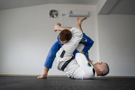 Photo for Brazilian jiu jitsu bjj training or sparing two athletes fighters dill martial arts technique at gym on the tatami mats wear kimono gi black belt instructor demonstrate submission armbar juji gatame - Royalty Free Image