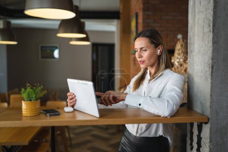 Téléchargez les photos : Une femme adulte mature caucasienne femme entrepreneur gestionnaire de travail utiliser tablette numérique tout en se tenant à la table à l'intérieur à la maison ou au travail porter chemise blanche copier l'espace - en image libre de droit