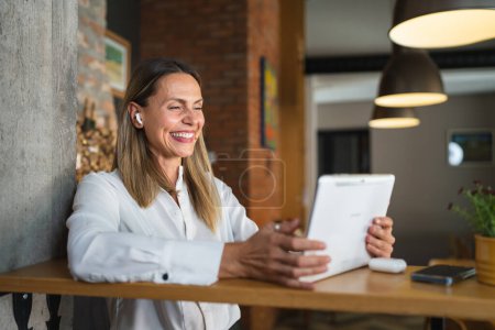 Téléchargez les photos : Une femme adulte mature caucasienne femme travail utiliser tablette numérique tout en se tenant à la table à l'intérieur à la maison ou au restaurant porter chemise blanche copie espace sourire heureux - en image libre de droit