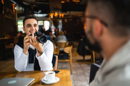 Foto de Un hombre utiliza la cámara digital sin espejo mientras se sienta en la cafetería o restaurante caucásico joven adulto fotógrafo tomando fotos trabajo persona real copia espacio - Imagen libre de derechos