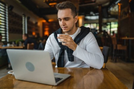 Un hombre caucásico adulto varón sentado en la mesa en el restaurante cafetería con computadora portátil para navegar por Internet o trabajar freelance remoto personas reales copiar espacio