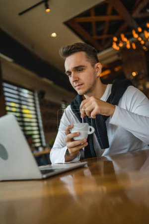 Téléchargez les photos : Un homme caucasien adulte mâle assis à la table au restaurant café en utilisant un ordinateur portable pour naviguer sur Internet ou travailler à distance freelance personnes réelles espace de copie inquiet - en image libre de droit