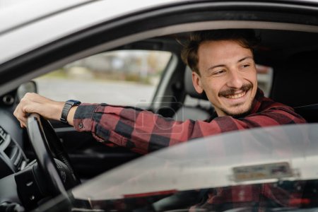 Téléchargez les photos : Un homme caucasien mâle avec les cheveux bruns et moustaches assis dans une voiture adulte conducteur porter chemise tout en conduisant concept de transport automobile personnes réelles copier l'espace sourire heureux - en image libre de droit