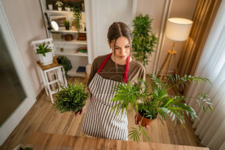 Téléchargez les photos : Une femme jeune caucasien femelle stand à la maison tenir fleurs plantes pot heureux sourire tour de taille vue de face jardinage et botanique horticulture soins concept copier l'espace - en image libre de droit