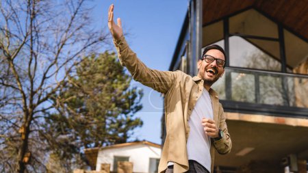 Photo for One man caucasian adult male stand outdoor in front of modern tiny house host or salesman with hands gesture invite in gesturing invitation happy smile in sunny day copy space - Royalty Free Image