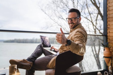 Photo for One man caucasian modern male sit on the balcony terrace alone at home wear shirt work on laptop computer in day remote happy smile confident success concept copy space thumb up gesture - Royalty Free Image