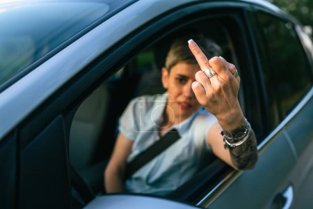 Foto de One woman senior mature female driver showing middle finger trough the window of the car mad angry furious pissed shows a negative gesture to the camera emotionally provocation and rude attitude - Imagen libre de derechos