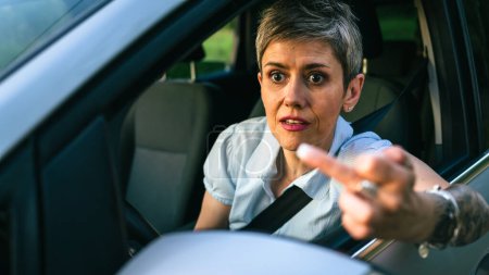Photo for One woman senior mature female driver showing middle finger trough the window of the car mad angry furious pissed shows a negative gesture to the camera emotionally provocation and rude attitude - Royalty Free Image