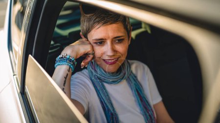 Téléchargez les photos : One mature woman caucasian female sitting on the back seat of the car looking trough the glass window in summer day happy smile travel and transport concept copy space real person gray short hair - en image libre de droit