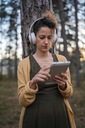 Téléchargez les photos : Une femme jeune femme caucasienne adulte se tient seule dans le parc ou la forêt dans la nature avec des écouteurs se préparant à la méditation guidée autosoin pratique concept d'équilibre émotionnel mental - en image libre de droit
