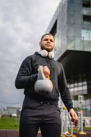 Photo for One man young caucasian male athlete stand outdoor in day posing with russian bell girya kettlebell weight real person copy space - Royalty Free Image