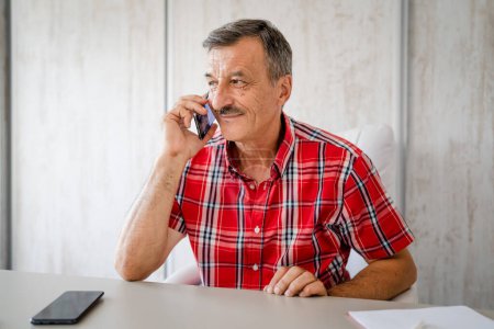 Photo for One man senior entrepreneur active caucasian male making a phone call talking while sitting at the desk table working at office manager and small business real people copy space - Royalty Free Image