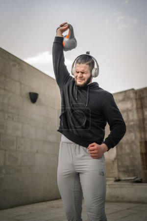 Foto de Un hombre joven atleta caucásico pie al aire libre en el entrenamiento de día con campana rusa girya kettlebell peso ejercicio persona real copiar espacio - Imagen libre de derechos