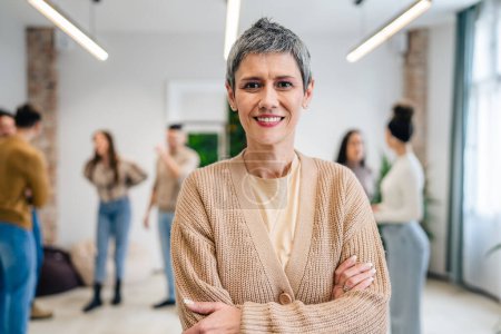 Photo for Portrait of senior woman in front of group of people men and women colleagues portrait of caucasian female stand at work happy smile confident with short gray hair copy space bright filter - Royalty Free Image