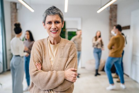 Photo for Portrait of senior woman in front of group of people men and women colleagues portrait of caucasian female stand at work happy smile confident with short gray hair copy space bright filter - Royalty Free Image
