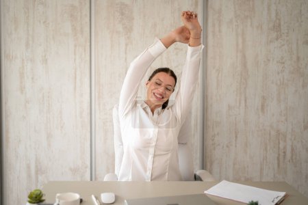 Foto de One woman female caucasian entrepreneur businesswoman or secretary sitting in office at desk at work stretching hands try to relax shoulders and back wear white shirt copy space - Imagen libre de derechos