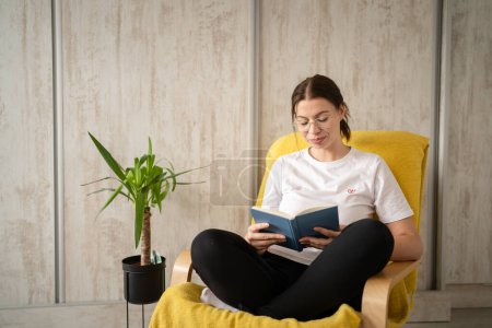Photo for One woman young adult caucasian female sitting in chair at home read book copy space front view real people leisure weekend concept looking to the book thinking contemplate - Royalty Free Image