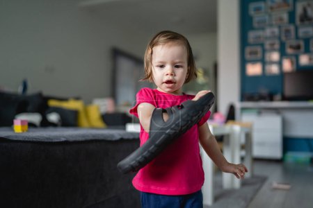 Photo for One caucasian toddler girl child playing with slippers at home in room alone copy space growing up and childhood development concept back view - Royalty Free Image