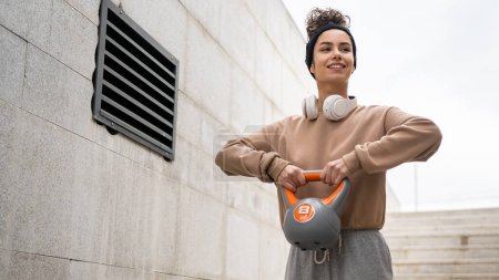 Una mujer joven atleta caucásica pie al aire libre en el entrenamiento de día con campana rusa girya kettlebell peso ejercicio persona real copiar espacio