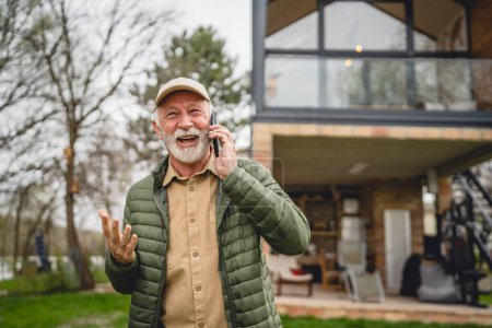 Photo for One man senior caucasian male with gray beard and cap stand outdoor in spring or autumn day happy smile use mobile smart phone to make a call talk happy smile copy space real people - Royalty Free Image