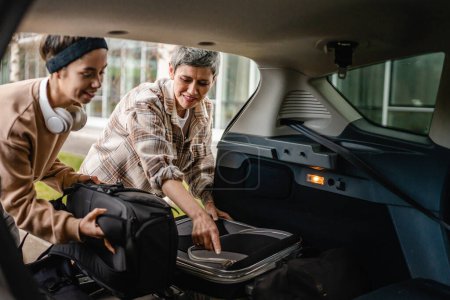 Photo for Two beautiful women student mother and daughter female travel concept take luggage baggage suitcase and other stuff belongings from back of car while moving into dormitory on college campus or travel - Royalty Free Image