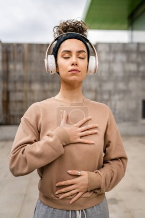 Photo for One woman adult caucasian female using headphones for online guided meditation practicing mindfulness manifestation with eyes closed stand outdoor real people self care concept copy space - Royalty Free Image