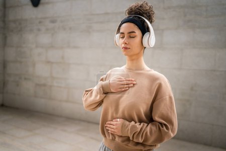 Photo for One woman adult caucasian female using headphones for online guided meditation practicing mindfulness manifestation with eyes closed stand outdoor real people self care concept copy space - Royalty Free Image