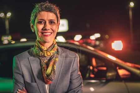 Photo for Portrait of one senior woman modern mature caucasian female with gray short hair stand in the city at night in front of the car real person copy space waist up - Royalty Free Image