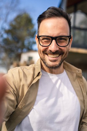 Téléchargez les photos : Un homme caucasien adulte moderne portrait d'homme avec barbe et lunettes heureux confiant à la maison autoportrait selfie UGC contenu généré par l'utilisateur - en image libre de droit